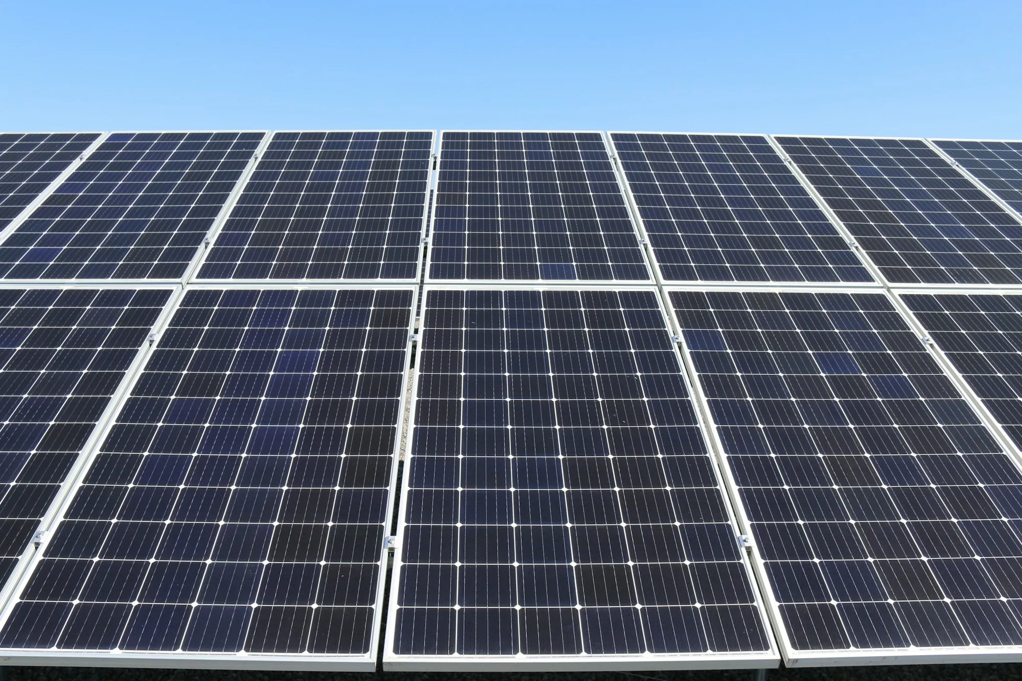 Grid of blue solar panels on a mounting rack under a clear sky
