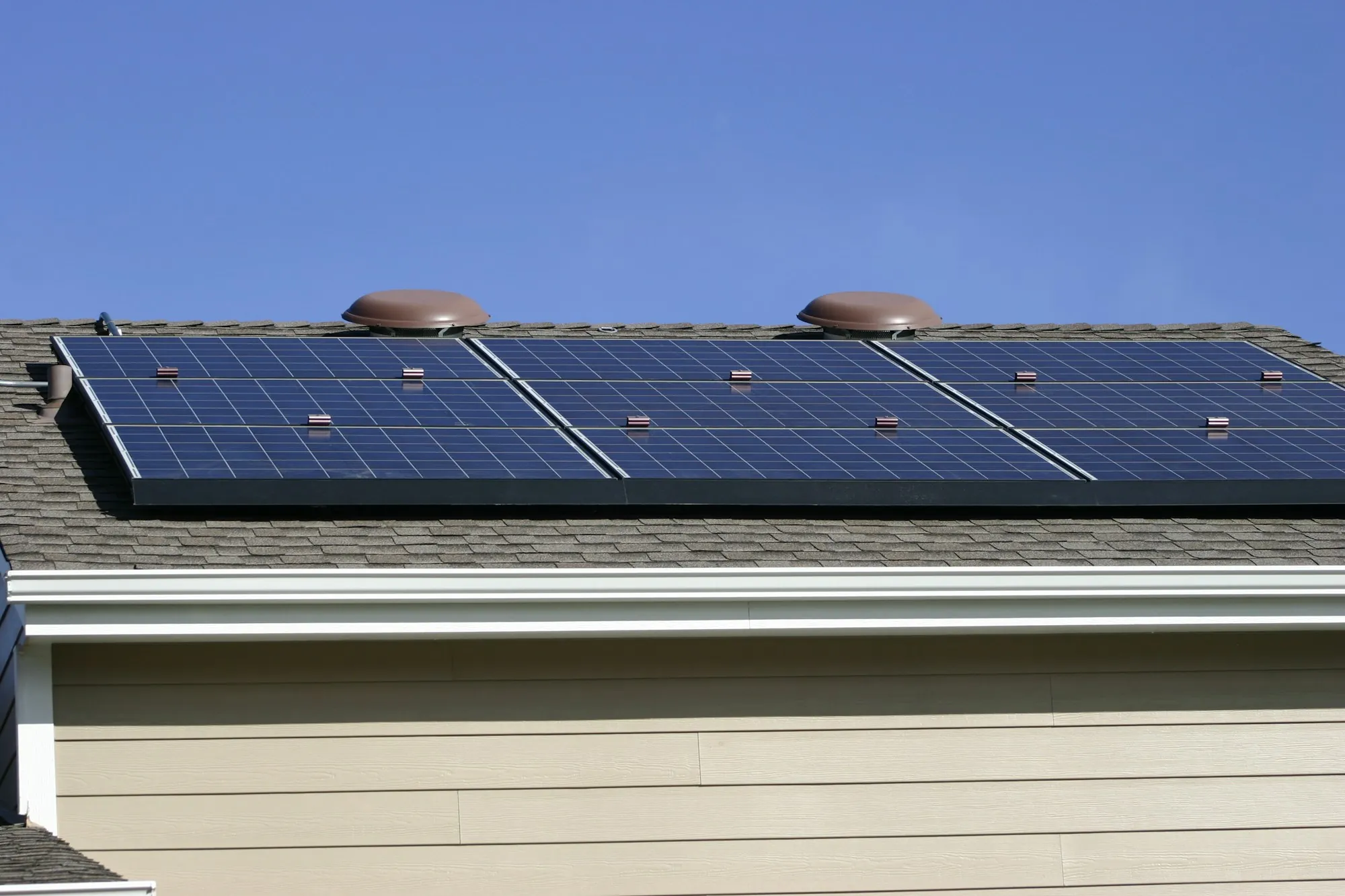 Row of blue solar panels on a gray shingle roof above a sided home