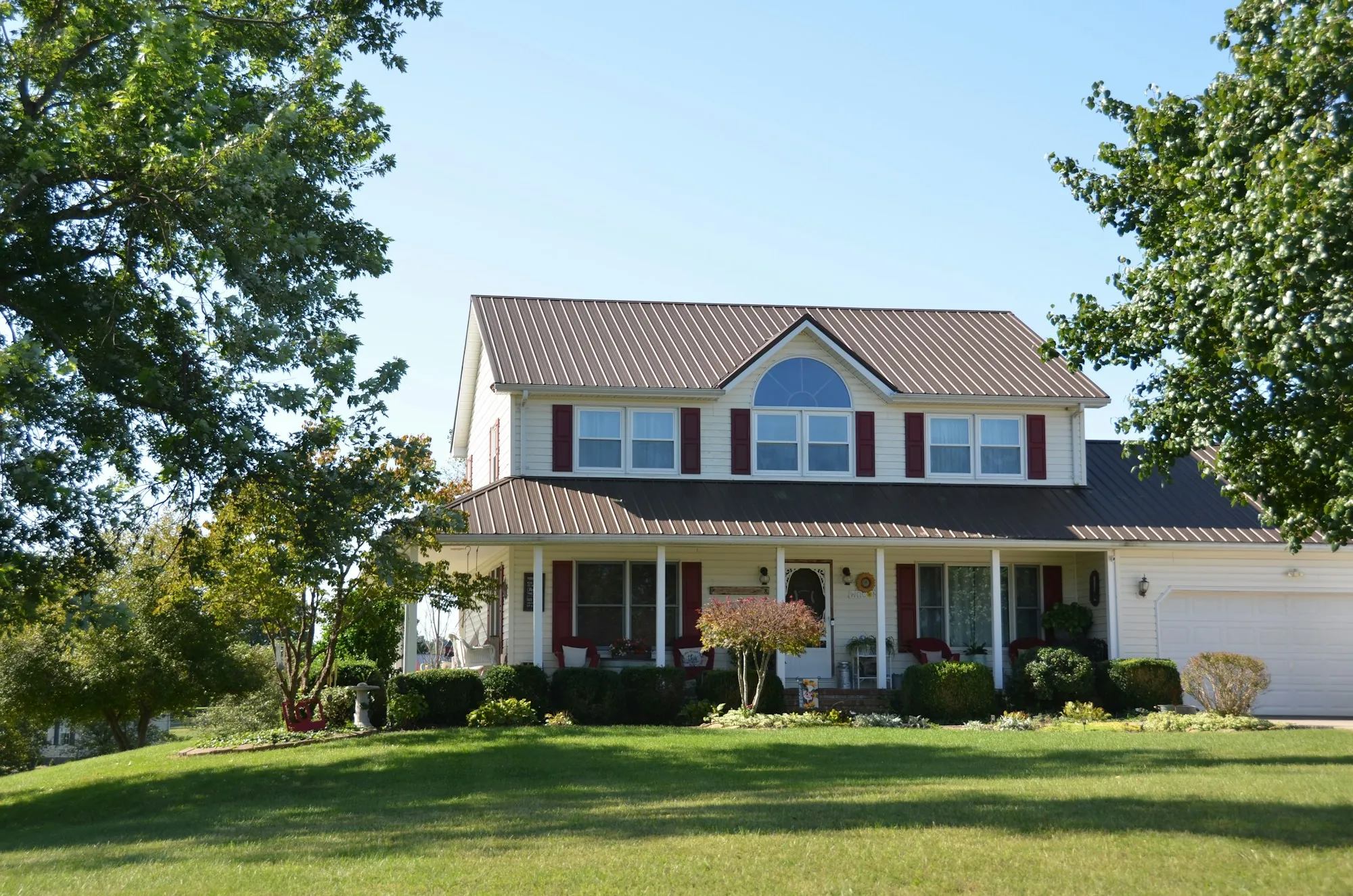 Two-story home with a red metal porch roof and a big green lawn
